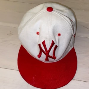 Vit och röd keps med broderad logga - Snygg keps i vitt och rött med broderad logga framtill. Kepsen har en röd skärm och detaljer i samma färg. Perfekt för en sportig look eller som en cool accessoar.