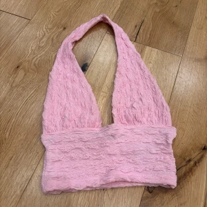 Rosa halterneck topp från H&M - Säljer en söt rosa halterneck topp med en texturerad yta. Toppen har en djup urringning och är perfekt för varma sommardagar. Den är mjuk och bekväm att bära.