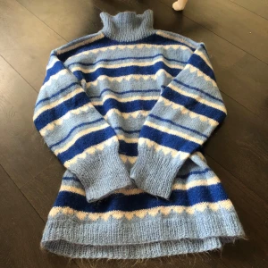 Blå randig egenstickad polotröja - Säljer en mysig blå egenstickad polotröja med randigt mönster i olika nyanser av blått och vitt. Håller värmen bra ❤️storlek…kanske S-M 😅