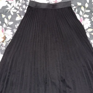Svart plisserad kjol - Elegant svart plisserad kjol med elastisk midja. Perfekt för en stilren look. Kjolen har en klassisk design som passar till många olika tillfällen.