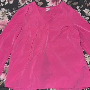 Rosa blus med v-ringning - Säljer en snygg rosa blus från H&M med v-ringning och öppen rygg. Blusen har tre kvarts ärmar och är perfekt för en färgglad look. Den är tillverkad i ett lätt och bekvämt material.