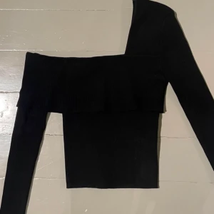 Svart offshoulder topp - Snygg svart offshoulder topp med långa ärmar och volangdetalj. Perfekt för en stilren look. Passar bra till både jeans och kjol.