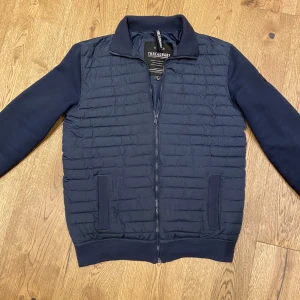 Mörkblå jacka från Threadbare - Säljer en snygg mörkblå jacka från Threadbare i storlek S. Jackan har en quiltad design på framsidan och dragkedja. Ärmarna är långärmade och har ribbade muddar. Perfekt för en stilren look. Använd 1 vår köptes från zalando för ca 1000kr och säljer den nu för 600kr Köparen står för frakt!!! Kan tänka mig att gå ner i pris vid smidig affär