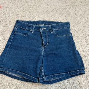 Mörkblå jeansshorts från &Denim - Klassiska mörkblå jeansshorts med normal passform och femficksdesign. Shortsen har bälteshällor, knapp och dragkedja framtill samt raka ben. Perfekta för sommardagar och enkla att matcha med olika toppar. Passar till storlek 152 fast den blir tajt då.