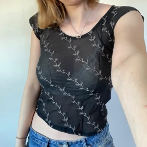 Mesh topp nygårsanna - Säljer en svart genomskinlig topp från My Garden med fina broderade blommor i vitt. Toppen har korta ärmar och en rund halsringning. Perfekt att styla med jeans eller kjol för en trendig look.