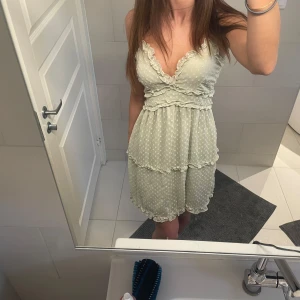 Ljusgrön prickig klänning från Vero Moda - Supersöt ljusgrön klänning med små vita prickar och volangdetaljer. Axelbandslös modell med omlott och v-ringning, perfekt för sommarens alla tillfällen. Lätt och luftig känsla i syntetmaterial.