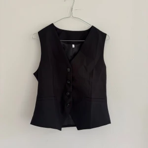 Svart kostymväst - Klassisk svart väst med v-ringning och fyra knappar framtill. Västen har en avslappnad passform och två dekorativa fickor framtill. Jag är en XS/S och den sitter oversized på mig