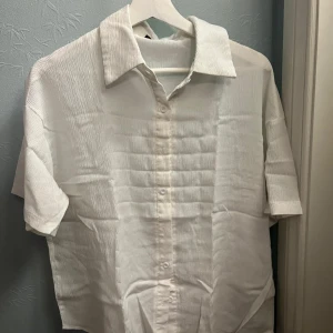 Vit kortärmad skjorta från SHEIN - Säljer en vit skjorta från SHEIN i storlek S (EU36). Skjortan har korta ärmar, klassisk krage och knäppning framtill. Materialet är lätt strukturerat och känns luftigt, perfekt för varmare dagar.