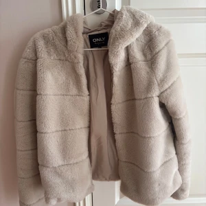 Beige pälsjacka med huva från ONLY - Säljer en supermjuk och fluffig beige pälsjacka från ONLY med huva och dragkedja. Jackan har lång ärm och är perfekt till våren. Enkel och stilren design som ger en lyxig känsla.💕