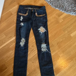 Lågmidjade jeans med detaljer - Säljer den här suuper coola jeansen då dem tyvärr är försmå. Jeansen har slit och guld detaljer och är lågmidjade. Skulle säga att dem är straight. Finns inget märke.