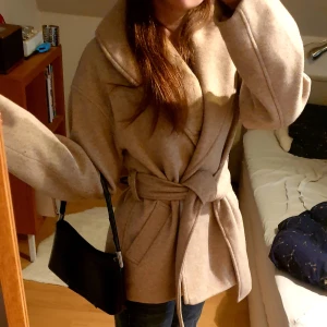 Beige kappa med bälte från Gina Tricot - Säljer en beige kappa från Gina Tricot i ullblandning. Jackan har bred krage, knytskärp i midjan och stora slag. Perfekt för höst och vår, med en stilren och tidlös design. Köptes på plick, men var tyvärr förstor så jag säljer nu vidare. Superfint skick! Skriv om det finns några frågor eller fler bilder❣