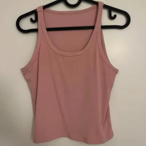 Rosa ribbad linnetopp - Säljer en ljusrosa ribbad linnetopp med breda axelband och rundad halsringning. Toppen är ärmlös och har en croppad passform, perfekt för varma dagar eller lager-på-lager. Supermjuk och stretchig i materialet.