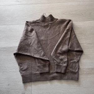 Brun polotröja i ullmix - Mysig brun polotröja med lång ärm och ribbade muddar. Tröjan har en hög krage och är tillverkad i ett mjukt ullmaterial som passar perfekt för kyligare dagar.