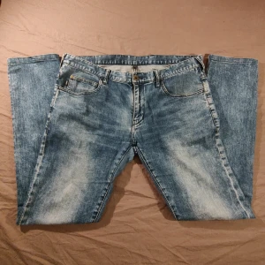 Blå jeans från Emporio Armani - Säljer ett par klassiska blå jeans från Emporio Armani med fem fickor och logga på bakfickan. Jeansen har normal passform och slimade ben, med snyggt tvättad finish och dragkedjegylf. Perfekta för en stilren look.