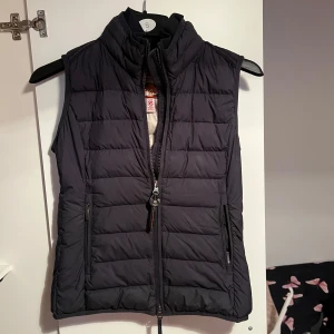 Svart dunväst från Parajumpers - Snygg svart dunväst från Parajumpers med hög krage och dragkedja framtill. Västen har två fickor med dragkedja och en ljus insida. Perfekt för lager-på-lager och har en sportig look.