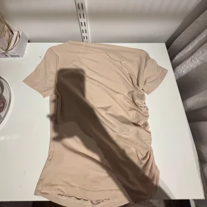 Beige t-shirt med rynkade detaljer - Säljer en beige t-shirt med korta ärmar och rynkade detaljer på ena sidan. Enkel och stilren design som passar perfekt till jeans eller kjol.