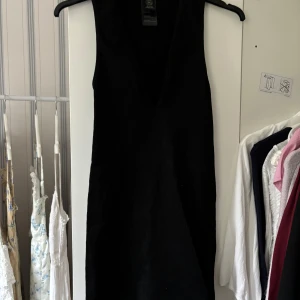 Svart ribbad ärmlös klänning - Säljer en svart, ärmlös klänning med djup v-ringning. Klänningen är ribbad och har en kroppsnära passform som framhäver siluetten. .