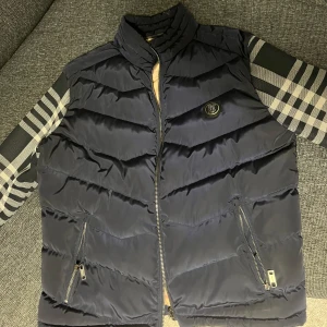 Burberry cardigan - Säljer en mörkblå cardigan från Burberry med klassiska rutiga ärmar i svart, grått och vitt. Västen har dragkedja framtill, två fickor med dragkedja och Burberry-mönster på insidan. Använt ett fåtal gånger.