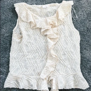 Vit volangväst från Gina Tricot - Säljer en söt vit väst från Gina Tricot med volangdetaljer längs krage, framkant och nederkant. Västen har ett lätt transparent, vågigt mönster och är perfekt för att lyfta en outfit med en romantisk touch.