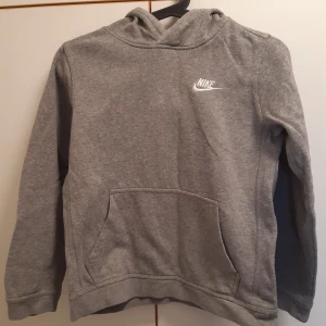 Grå hoodie från Nike - Säljer en klassisk grå hoodie från Nike med vit logga på bröstet. Tröjan har huva och en stor magficka framtill. Perfekt för en avslappnad stil och enkel att matcha med det mesta.