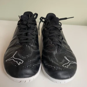 Svarta inomhusfotbollsskor från Puma - Säljer ett par svarta inomhusfotbollsskor från Puma .Har använt dessa skor få tal gånger.Skorna har snörning och en vit platt sula som ger bra grepp på inomhusplaner. Perfekta för dig som gillar futsal eller inomhusträning.Ny pris är 600kr.