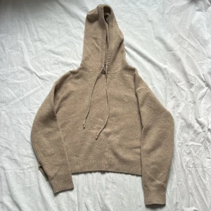 Beige hoodie i ull från Polo Ralph Lauren - Stickad hoodie från Polo Ralph Lauren i mjuk ullmix. Tröjan har långa ärmar, ribbade muddar och huva. Klassisk broderad logga på bröstet och slits i sidan. Färgen på hoodien blev lite ljusare i kameran men första och sista bilden visar rätt färg. Helt ny, aldrig använd. 