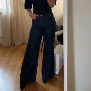 Mörkblå wide leg jeans - Säljer ett par mörkblå jeans med hög midja och vida ben. Klassisk femficksmodell med knapp och dragkedja framtill. Perfekta för en trendig och avslappnad look. Aldrig använda.