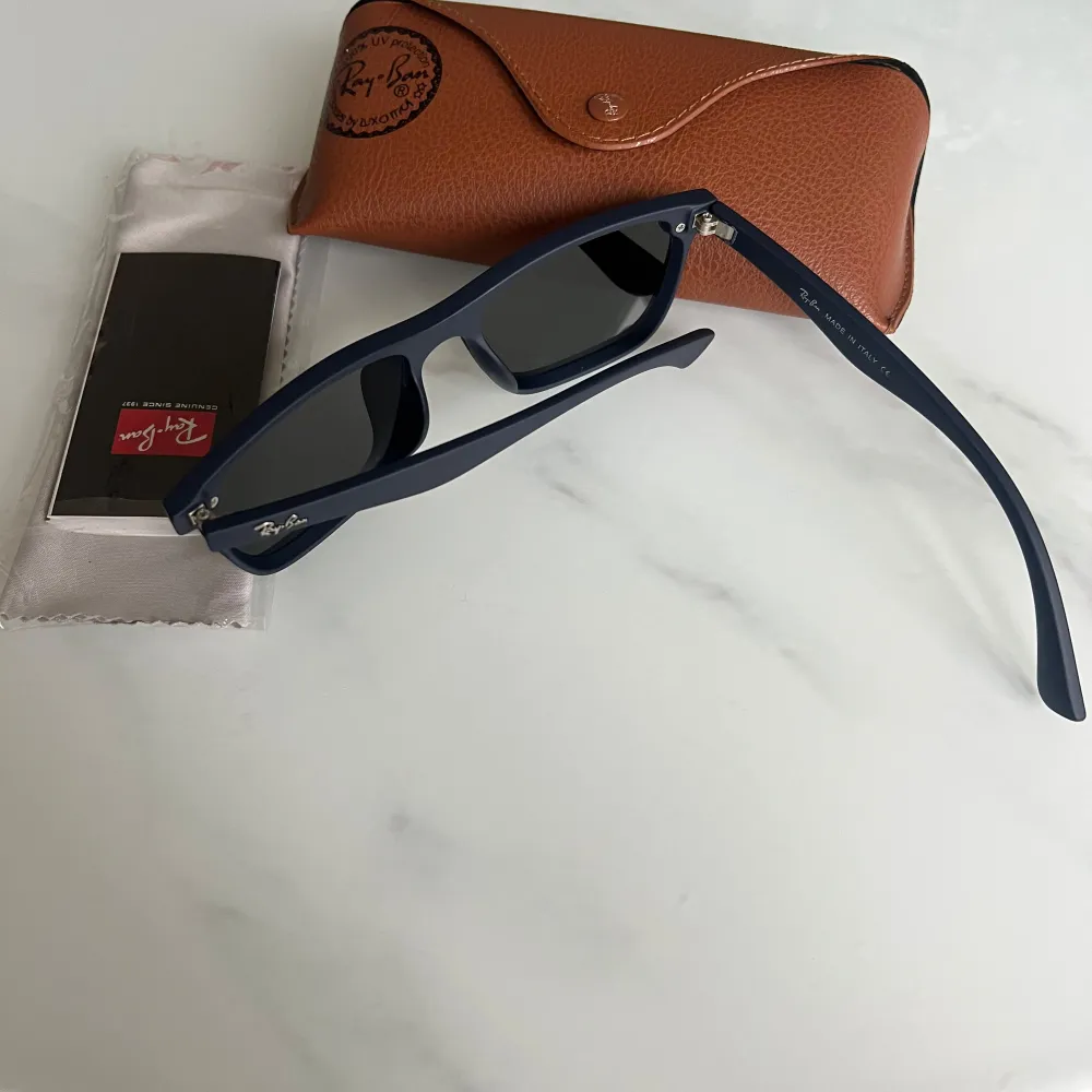 Klassiska svarta Wayfarer solglasögon från Ray-Ban med mörka glas och tydlig logga på skalmen. Säljs med original brunt fodral och putsduk. Perfekt accessoar för soliga dagar.. Asusteet.