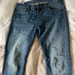 Levi's 501 jeans blå denim - Klassiska blå Levi's 501 jeans med raka ben och knappgylf. Jeansen har fem fickor och en vintage look. Perfekta för dig som gillar tidlös denimstil.