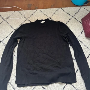 Svart polotröja - En klassisk svart polotröja med lång ärm. Perfekt basplagg som passar till många olika stilar. Tröjan har en hög krage och är tillverkad i ett mjukt material.