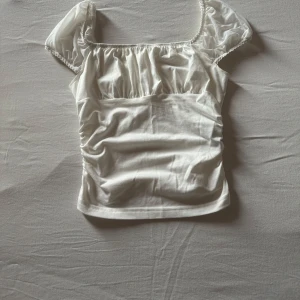 Vit topp med puffärmar - Säljer en söt vit topp med puffiga korta ärmar och rynkade detaljer framtill. 