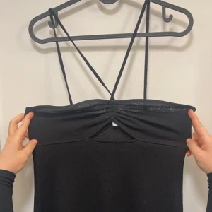 Svart axelbandslös klänning med smala band - Säljer en svart klänning med smala axelband som korsas i ryggen. Klänningen har en lätt rynkad detalj framtill vid bysten och är axelbandslös. Enkel och stilren modell som passar perfekt till sommarens tillfällen.