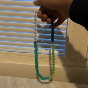 Färgglatt pärlhalsband i blått, grönt och transparent - Säljer ett handgjort halsband med stora pärlor i blått, grönt och transparent. Perfekt för dig som vill ha en färgklick till din outfit. Halsbandet har en enkel och lekfull design.