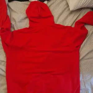 Säljer en röd hoodie från Champion med tryck på bröstet där det står 'New York Champion Since 1919'. Tröjan har huva med vita snören och en stor magficka. Perfekt för en avslappnad stil.
