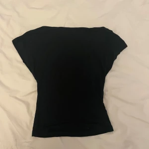 Svart tight topp - En enkel svart topp med tight passform och korta ärmar. Toppen har en öppen rygg och är tillverkad i ett mjukt material som sitter skönt mot kroppen. Perfekt att matcha med jeans eller kjol.