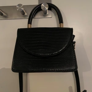 Svart minihandväska  - En svart mini handväska (rymmer en mobil på längden ungefär) Väskan har en avtagbar axelrem (se bild 2). Perfekt nu till balen 🙌