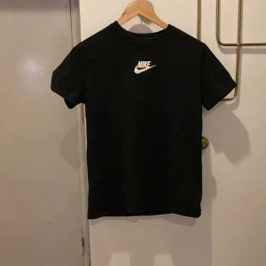 Svart t-shirt från Nike - Svart t-shirt från Nike med klassisk vit logga på bröstet. Modellen är loose fit och har rund halsringning samt korta ärmar. Perfekt för en avslappnad och sportig stil.