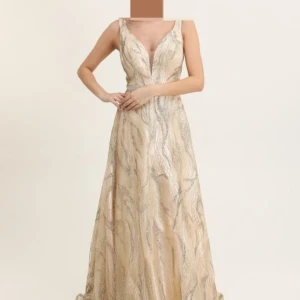 Champagnefärgad långklänning med glitter och djup v-ringning - Säljer en elegant champagnefärgad långklänning med glittriga detaljer och djup v-ringning! Klänningen har markerad midja med glittrigt band och är ärmlös. Perfekt för bal eller festliga tillfällen. Materialet är skimrande och ger en lyxig känsla.  Den är helt OANVÄND MED KVITTO och PRISLAPP.😋 Jag köpte för 3500kr men säljer den för mindre än hälften.💕 Kan pruta på priset.