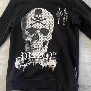 Phillip plein sweatshirt S/M - Cool svart sweatshirt från Philipp Plein med stor vit dödskalle och texten 'FALL-WINTER' framtill. Tröjan har långa ärmar och tryckdetaljer på bröstet. Perfekt för dig som gillar streetwear och vill sticka ut.