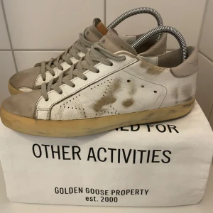 Vita sneakers från Golden Goose - Säljer ett par vita sneakers från Golden Goose med grå detaljer och beige sula. Skorna är perfekta för dig som gillar en unik, cool stil på skor. 100% autentiska.