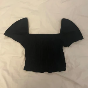 Svart croppad topp med puffärmar - Trendig svart croppad topp med fyrkantig ringning och stora puffärmar. Toppen är ribbad och har en tight passform, perfekt för att lyfta din outfit med en cool touch.