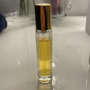 Tom Ford parfymflaska med guldlock - Elegant parfymflaska från Tom Ford med räfflad, transparent glasdesign och ett glänsande guldlock. Flaskan är fylld med en gyllengul parfymvätska och har en lyxig känsla som passar perfekt för dig som gillar exklusiva dofter.