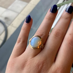 Guldfärgad ring med opalsten, ”opalit” - Säljer en snygg guldfärgad ring med en rund, skimrande opalsten i mitten. Ringen har en elegant och enkel design som verkligen framhäver stenen. Perfekt för dig som vill ha något unikt och stilrent!