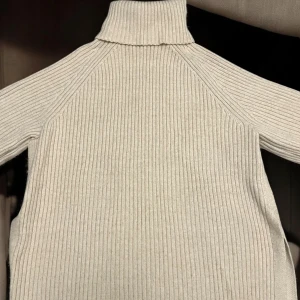 Tjock stickad halströja – beige & oversize (M, passar L/XL) - Jättemysig beige halströja i stickad modell. Oversize fit – står som M, men sitter lika snyggt på L och XL också! Perfekt för kyligare dagar, supermjuk och riktigt skön att ha på sig. Stilren färg som funkar till allt.