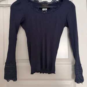 Mörkblå ribbad topp med spets från Rosemunde - Säljer denna  mörkblåa långärmade toppen från Rosemunde med ribbad struktur och fina spetsdetaljer vid halsringning och ärmslut.