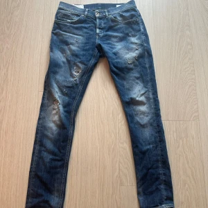 Blå Dondup George jeans med slitningar - Säljer ett par klassiska blå jeans med slitningar och lätt tvättad look. Byxorna har normal passform, fem fickor och stängs med dragkedja och knapp. Perfekta för en avslappnad stil. Tror jag Har tags och kvitto kvar.