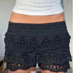 Svarta spets shorts - Snygga svarta shorts med spetsdetaljer och volanger. Perfekta för en somrig look. De har en elastisk midja för bekväm passform.