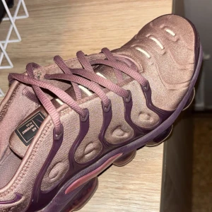 Nike Air Vapormax Plus i rosa och lila - Nike Air Vapormax Plus sneakers i en snygg mix av rosa och lila nyanser. Skon har en unik vågig design på ovandelen, genomskinlig sula med synliga luftbubblor och matchande snörning. Perfekt för dig som vill sticka ut med dina sneakers.