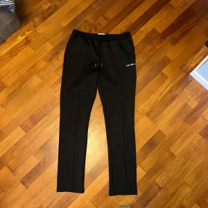 Svarta byxor från Les Deux med snörning - Svarta byxor från Les Deux med dragsko i midjan och diskret logga på vänster lår. Byxorna har raka ben och är perfekta för en stilren och avslappnad look.