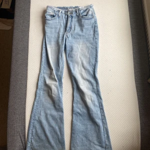 Ljusblå flared jeans från H&M - Säljer ett par ljusblå jeans från H&M med flared ben och rå kant upptill. Jeansen har justerbar midja och klassisk femficksdesign. Perfekta för dig som gillar en retroinspirerad look med extra vidd nertill.